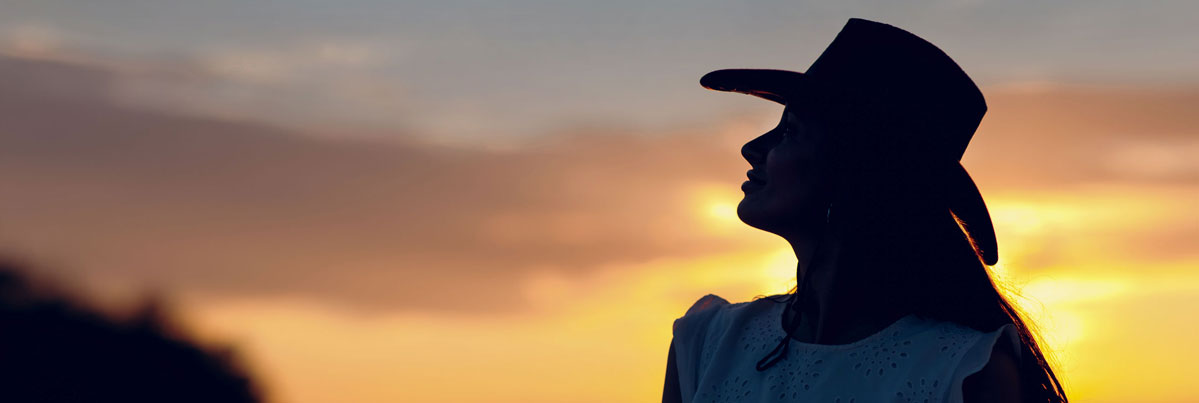 woman wearing hat silhouetted againset sunset